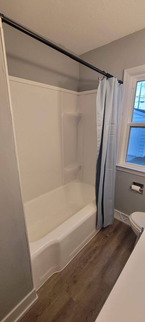 bathroom with shower / bath combo, toilet, and wood finished floors