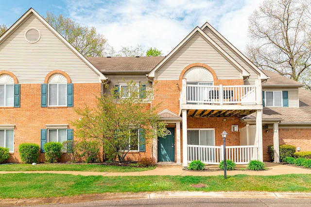 view of front of home featuring covered porch, a front lawn, brick siding, and a balcony