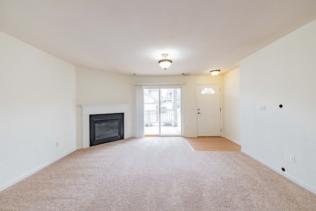 unfurnished living room with light colored carpet, baseboards, and a glass covered fireplace