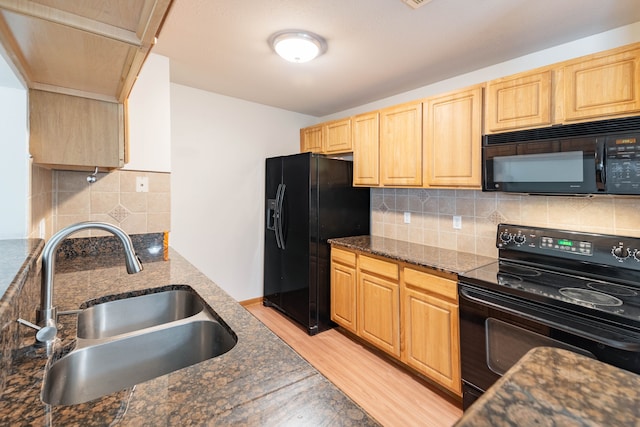 kitchen with a sink, light brown cabinets, light wood-style flooring, backsplash, and black appliances