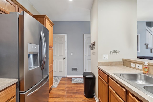 kitchen featuring visible vents, light wood-type flooring, light countertops, stainless steel fridge with ice dispenser, and a sink