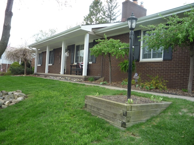 exterior space featuring a porch, brick siding, a chimney, and a front lawn
