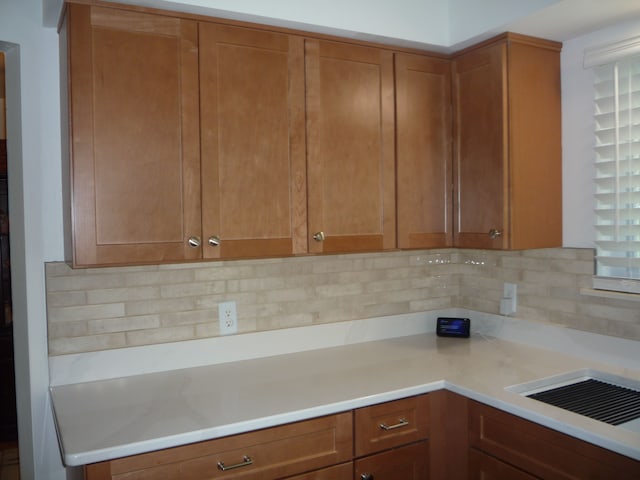 kitchen featuring light countertops, decorative backsplash, brown cabinets, and a healthy amount of sunlight