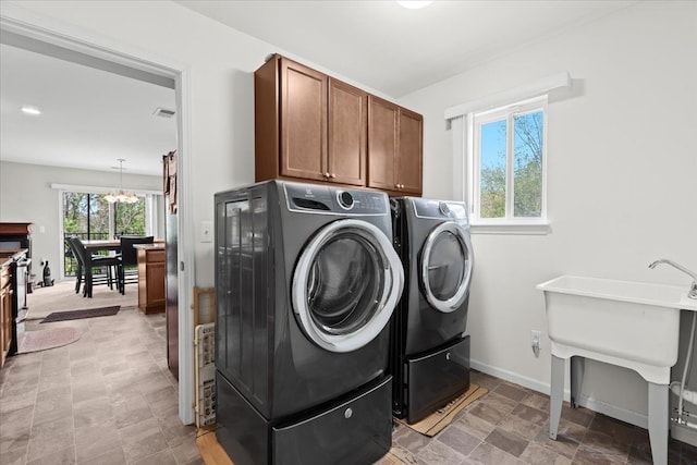 washroom with cabinet space, a notable chandelier, a sink, visible vents, and washing machine and dryer