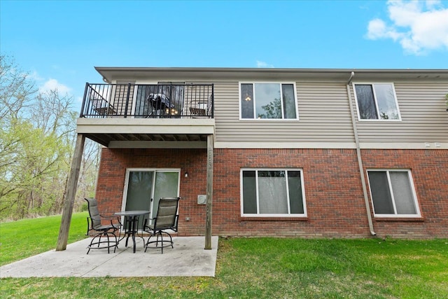 rear view of property featuring a yard, brick siding, a balcony, and a patio area