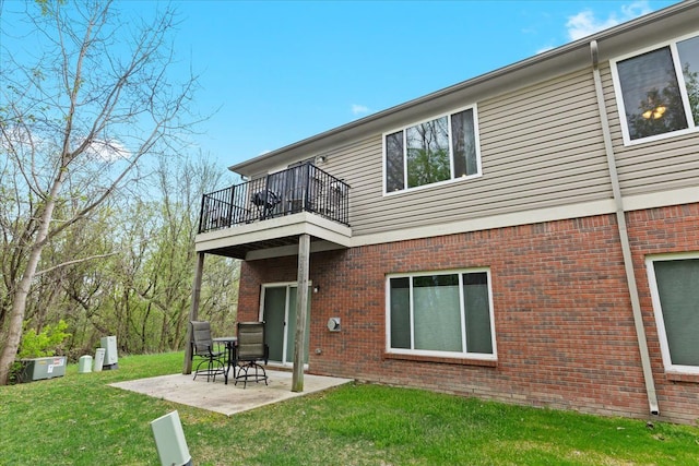 rear view of house featuring brick siding, a lawn, a balcony, and a patio