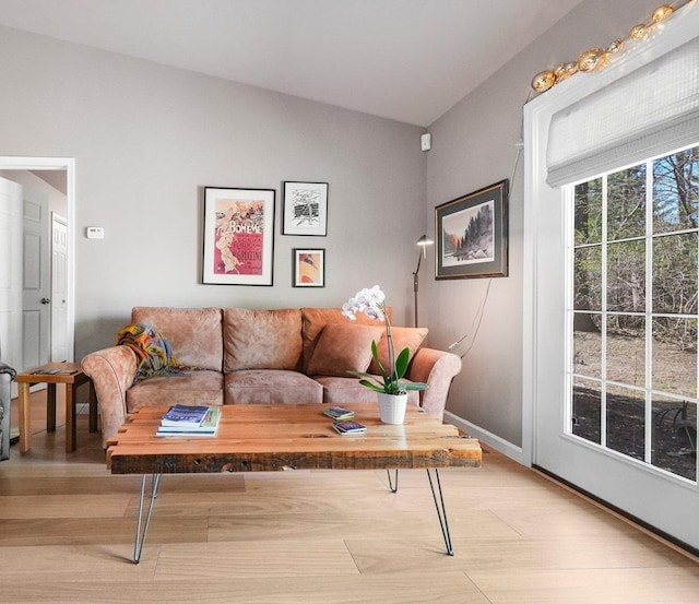 living area with baseboards, light wood finished floors, and lofted ceiling