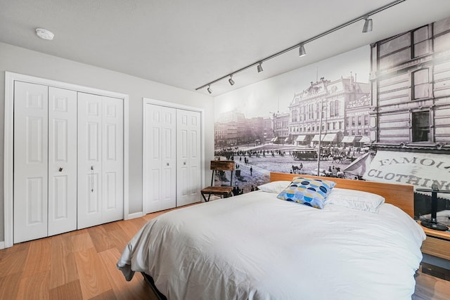 bedroom featuring track lighting, two closets, and wood finished floors