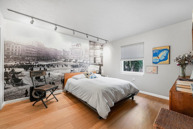 bedroom with baseboards, track lighting, and wood finished floors