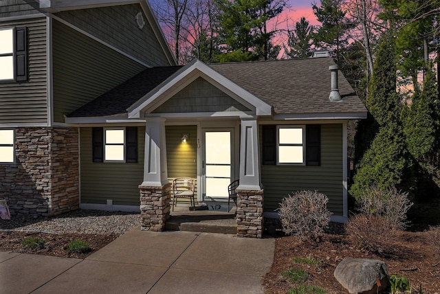 exterior space featuring covered porch, roof with shingles, and stone siding