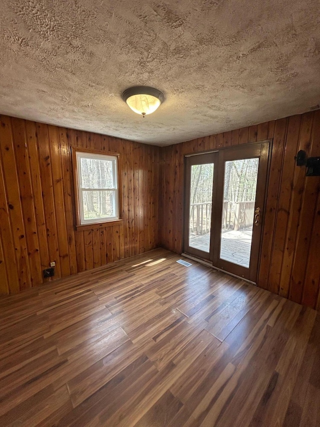 757 E Sidney Rd, Stanton, MI 48888 - unfurnished room featuring wooden walls, a textured ceiling, wood finished floors, and visible vents