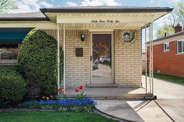 view of exterior entry featuring covered porch and brick siding