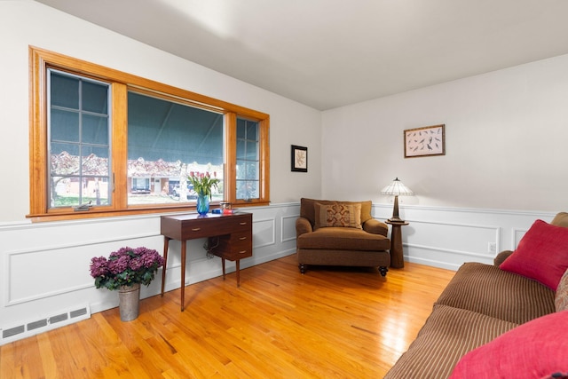 living area with a decorative wall, visible vents, a wainscoted wall, and light wood-type flooring