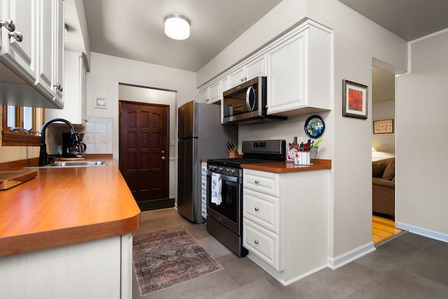 kitchen featuring a sink, baseboards, stainless steel appliances, and white cabinetry