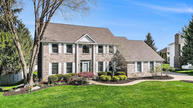 view of front of house with fence, a shingled roof, brick siding, and a front yard