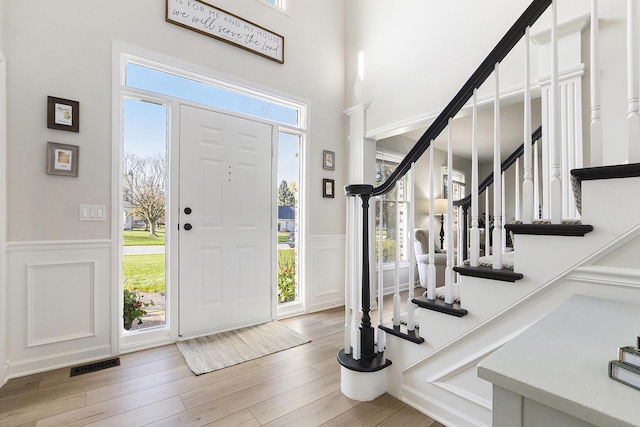entryway with visible vents, stairs, wood finished floors, a decorative wall, and a wainscoted wall
