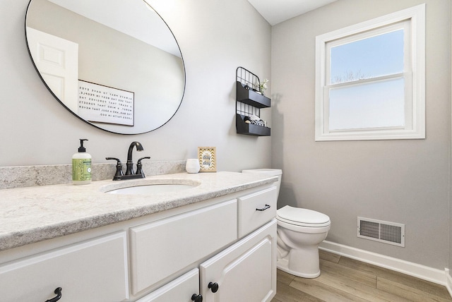 bathroom featuring visible vents, wood finished floors, vanity, baseboards, and toilet
