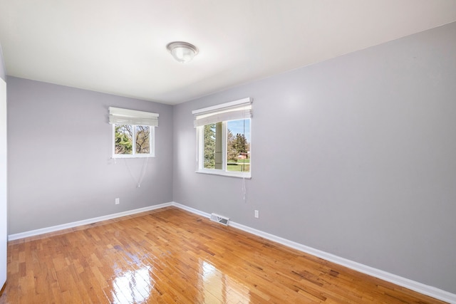 empty room featuring baseboards, visible vents, and light wood finished floors