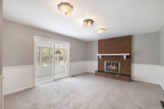 unfurnished living room with a wainscoted wall, a brick fireplace, carpet floors, and visible vents