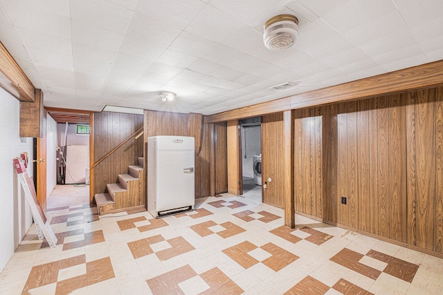 finished below grade area featuring washer / clothes dryer, stairway, freestanding refrigerator, wooden walls, and light floors