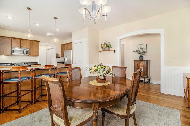 8 Georgia Ct, Pentwater, MI 49449 - dining area featuring arched walkways, a chandelier, wainscoting, and light wood-style flooring