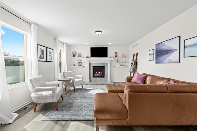 living area featuring a tiled fireplace, wood finished floors, a healthy amount of sunlight, and visible vents