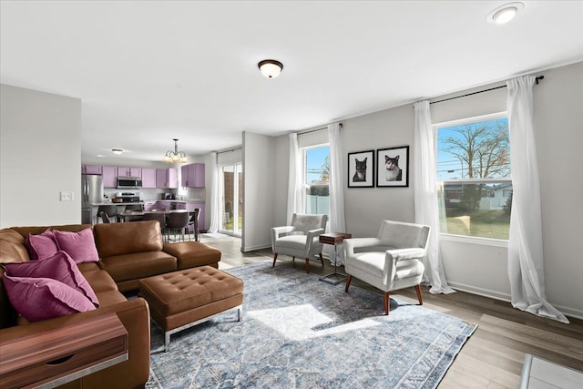 living area with plenty of natural light, baseboards, an inviting chandelier, and light wood-type flooring