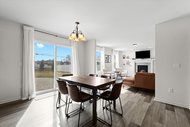 dining space featuring baseboards, a notable chandelier, wood finished floors, and a tile fireplace
