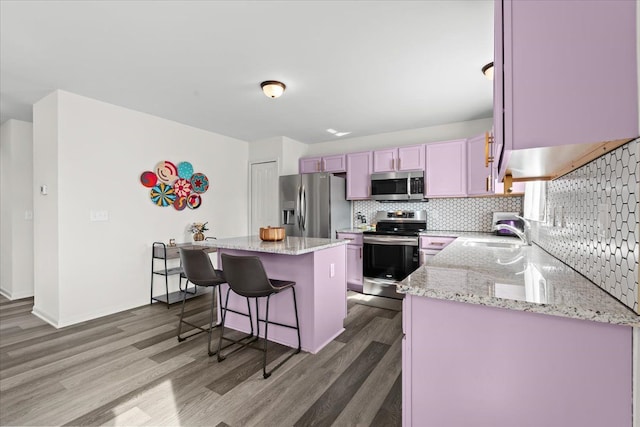 kitchen featuring a breakfast bar, a sink, stainless steel appliances, wood finished floors, and a kitchen island