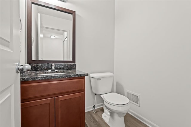 half bathroom with visible vents, wood finished floors, vanity, baseboards, and toilet