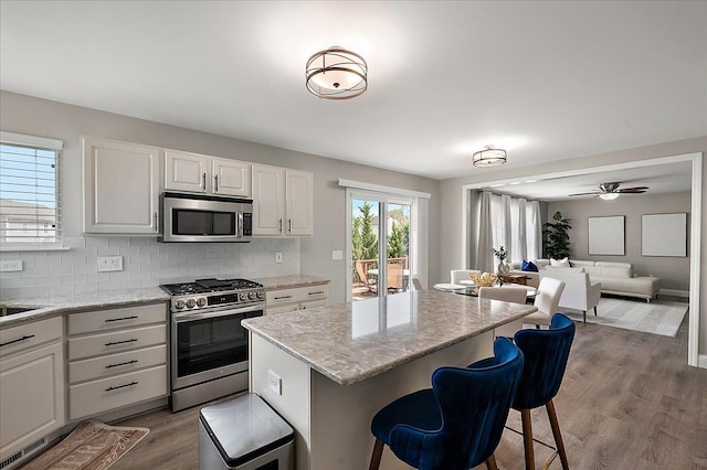 kitchen featuring white cabinets, appliances with stainless steel finishes, a breakfast bar, dark wood finished floors, and decorative backsplash