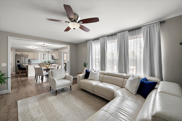 living room with baseboards, ceiling fan, and light wood finished floors