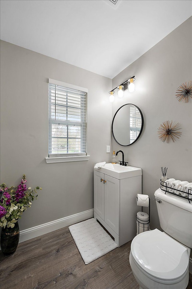 half bath with baseboards, vanity, toilet, and wood finished floors