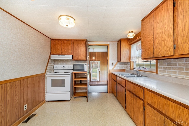 kitchen featuring brown cabinets, a sink, white appliances, tasteful backsplash, and under cabinet range hood