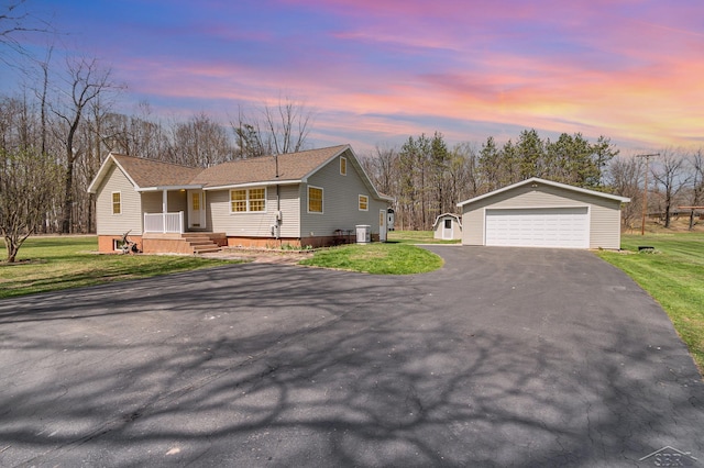 ranch-style home featuring a shingled roof, covered porch, a detached garage, a lawn, and an outdoor structure