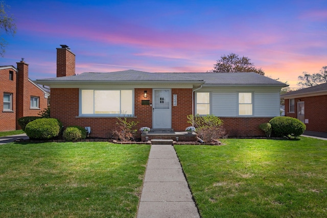view of front of property with a lawn, a chimney, and brick siding