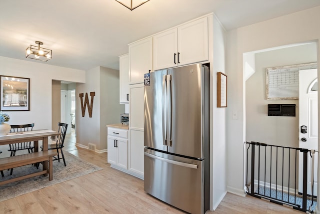 kitchen featuring visible vents, light wood-type flooring, baseboards, freestanding refrigerator, and white cabinetry