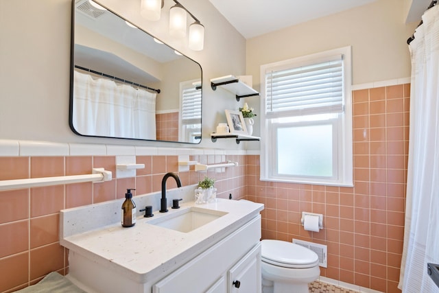 full bathroom with tile walls, vanity, toilet, and visible vents