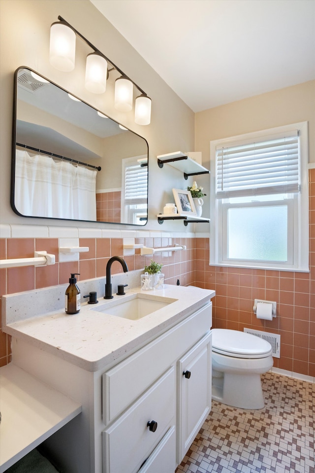 bathroom with visible vents, vanity, a healthy amount of sunlight, toilet, and tile walls