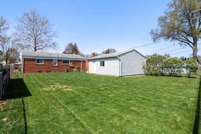 rear view of property featuring a lawn, fence, an outdoor structure, and brick siding