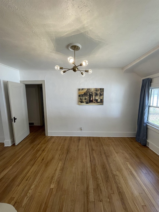 unfurnished dining area featuring baseboards, a textured ceiling, wood finished floors, and a chandelier