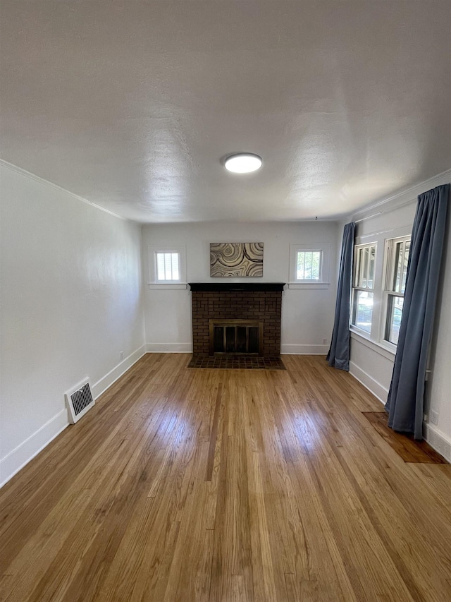 unfurnished living room with a healthy amount of sunlight, visible vents, a brick fireplace, wood finished floors, and baseboards