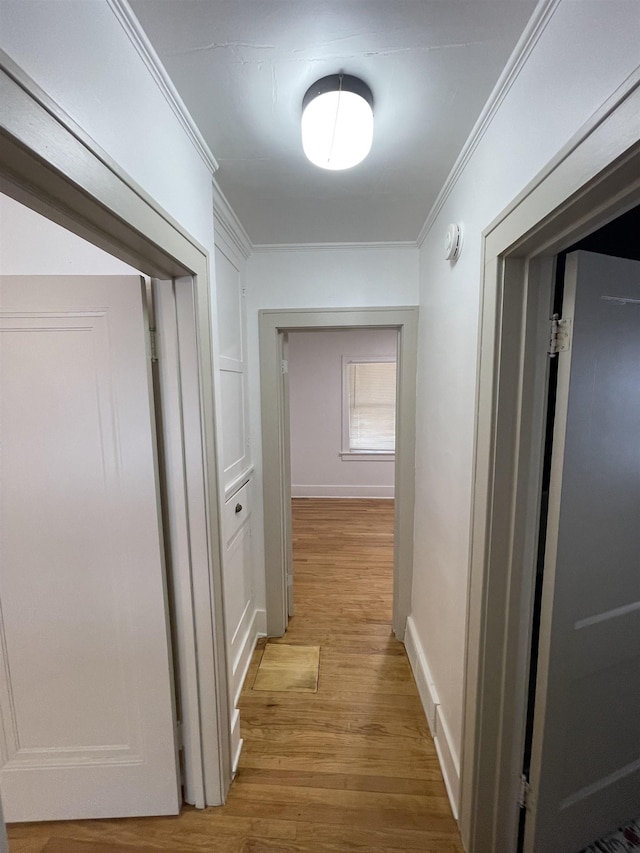 hallway featuring crown molding, baseboards, and light wood-style flooring
