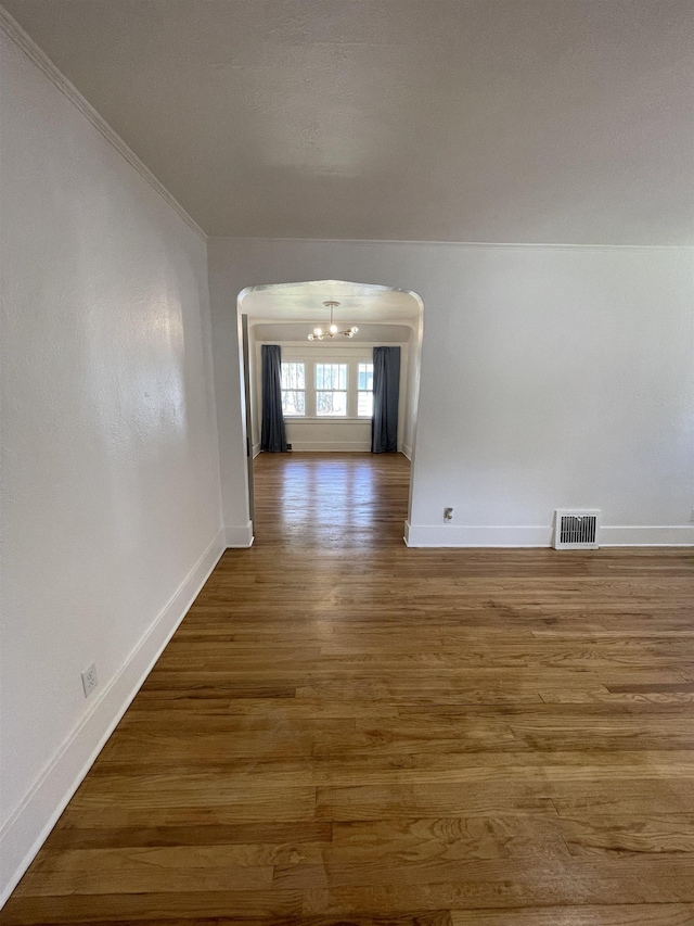 corridor with arched walkways, a chandelier, baseboards, wood finished floors, and visible vents