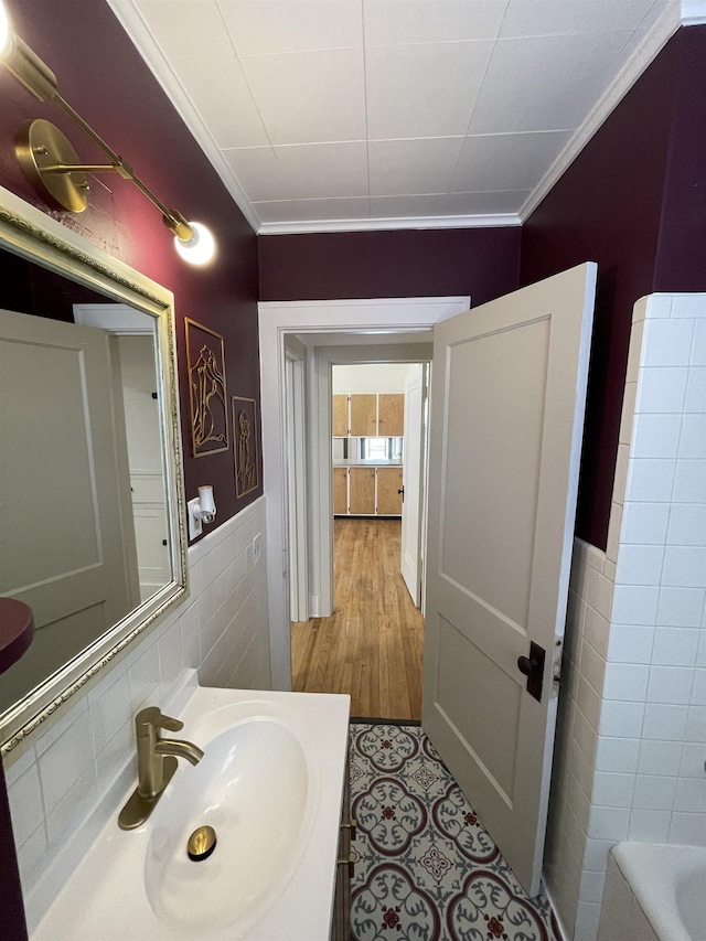 bathroom featuring crown molding, tile walls, a sink, a bathing tub, and a wainscoted wall