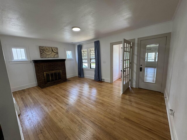 2314 Begole St, Flint, MI 48504 - unfurnished living room featuring wood finished floors, healthy amount of natural light, a brick fireplace, baseboards, and a textured ceiling