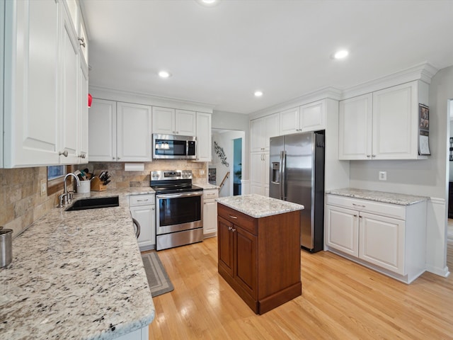 kitchen featuring light wood-style floors, white cabinets, a sink, appliances with stainless steel finishes, and backsplash
