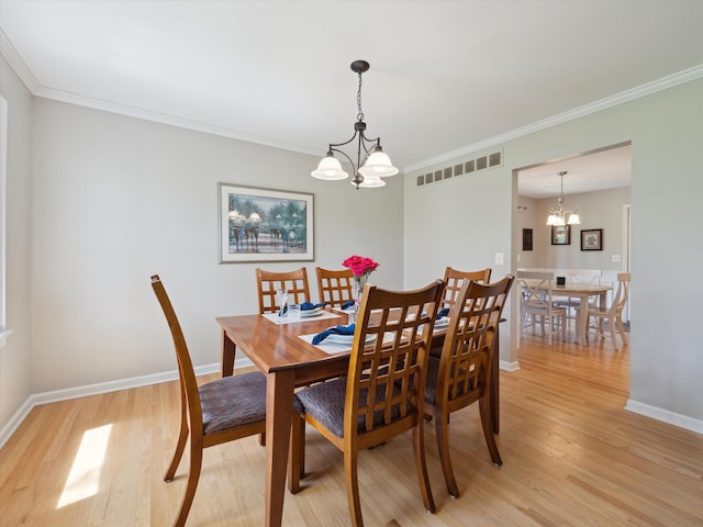 dining room featuring crown molding, a chandelier, light wood finished floors, and visible vents
