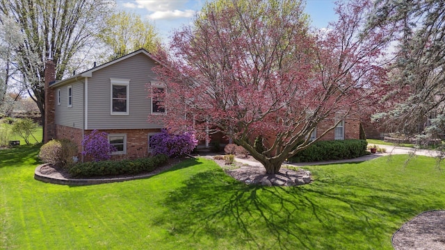 view of side of home with a chimney, a yard, and brick siding