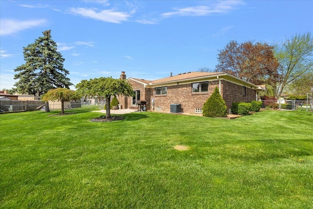 back of property with central air condition unit, brick siding, fence, a yard, and a patio